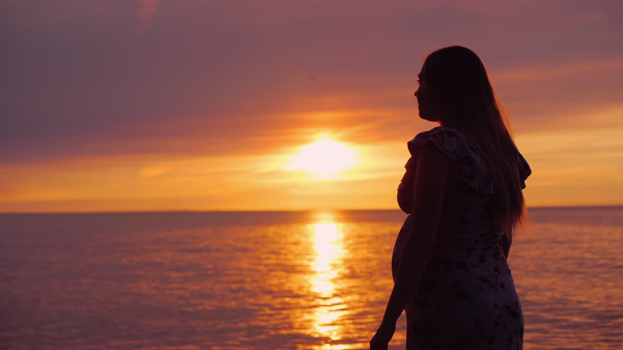 바다 위의 일몰을 배경으로 임신한 아내의 손을 잡고 있는 아시아 남자의 측면