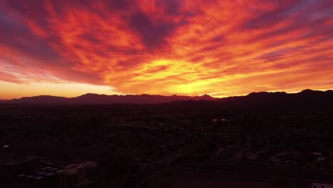 Vista-Aérea-De-Una-Puesta-De-Sol-De-Fuego-Sobre-Las-Montañas-Estrella-Y-La-Montaña-Sur-Cerca-De-Tempe-Arizona,-Nubes-Rojas-Amarillas-Anaranjadas