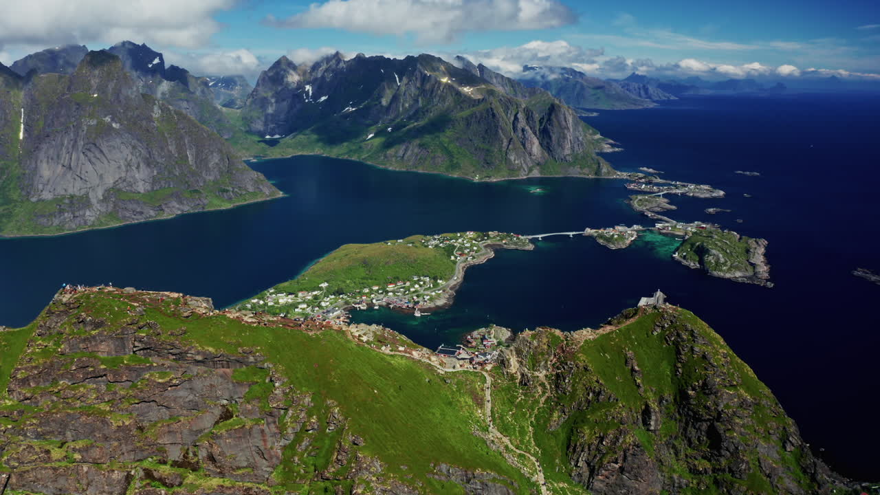 Aerial drone shot over Reinebringen, Reine, Lofoten Islands, Norway.
High view of the picturesque green landscape. View of the fjords and blue nordic sea. Touristic attraction for hiking activities.