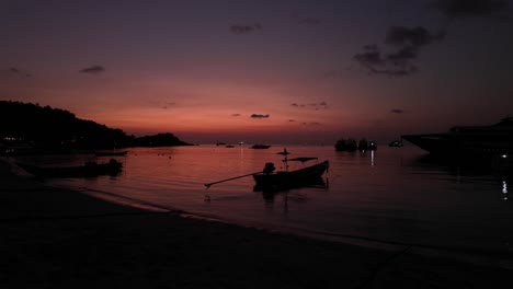 multiple boats moored in sheltered beach on tropical island, shot during beautiful pink and orange sunset