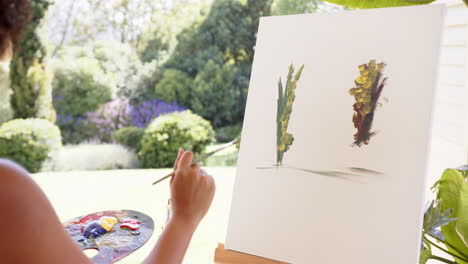 creating outdoor nature artwork, person painting on canvas with paintbrush and palette