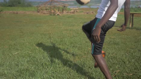 tiro de cerca en cámara lenta de las piernas de un joven hombre africano mientras patea con una pelota de fútbol en un campo de hierba