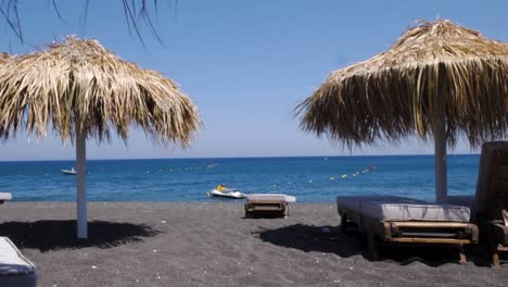 Handheld-Wide-Shot-of-Perissa-Beach-in-Santorini-Greece,-With-Black-Lava-Sand-on-a-Sunny-Summer-Day