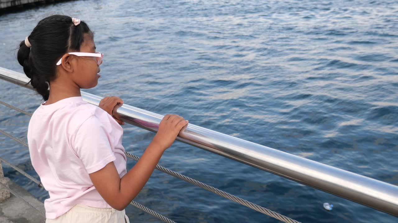 Junges Mädchen zeigt vom Steg aus auf Müll im Wasser