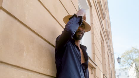 afro caribbean man putting his panama hat on while leaning on the wall with one leg up in the old town street 2