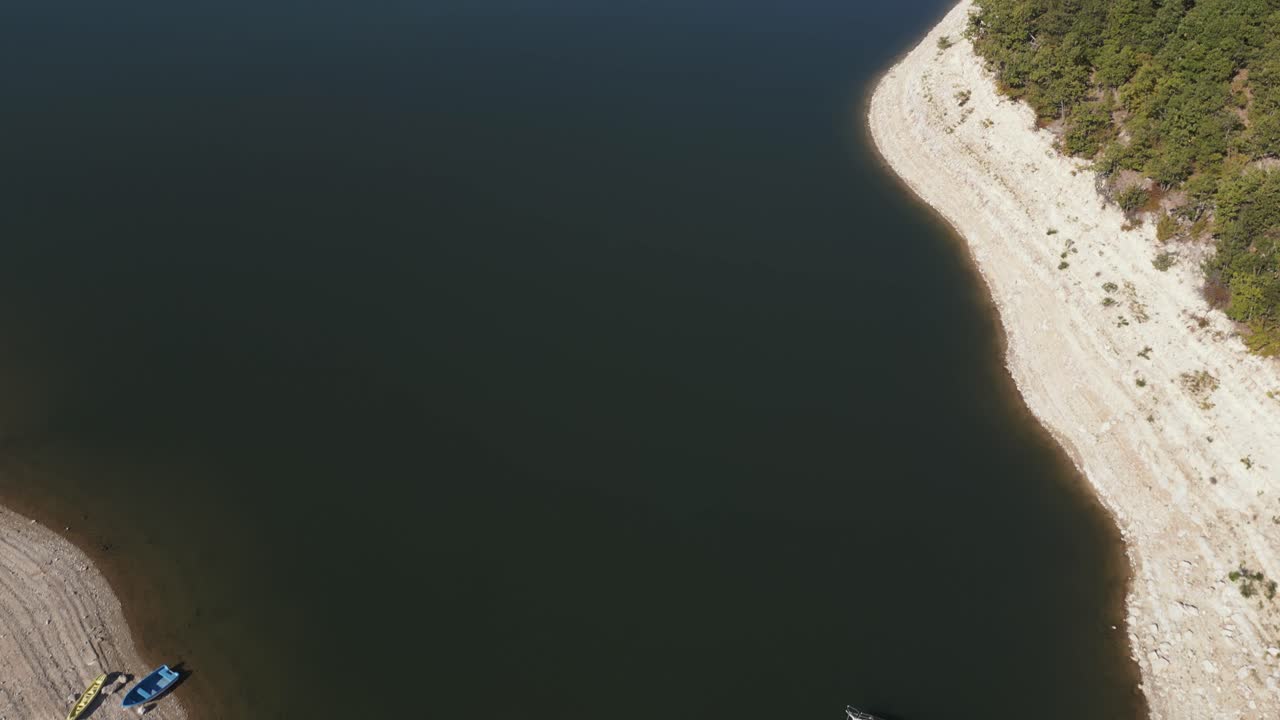 Aerial shot of a small boat docked along the sandy shore of a dam, with clear water and a peaceful surrounding