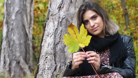 Brunette-girl-in-the-autumn-forest-holds-a-yellow-leaf-in-her-hand-and-spins-it-and-hide-her-face