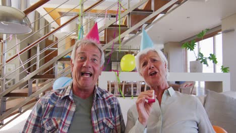 senior caucasian couple blowing party blowers celebrating birthday enjoying at home