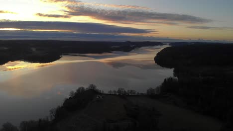 Aerial-view-at-evening-of-an-orange-sunset-reflecting-on-a-lake,-peaceful-background