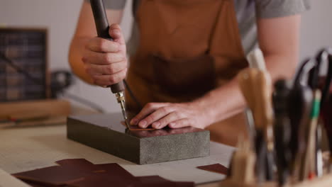 leathersmith polishes leather edge with tool at workplace