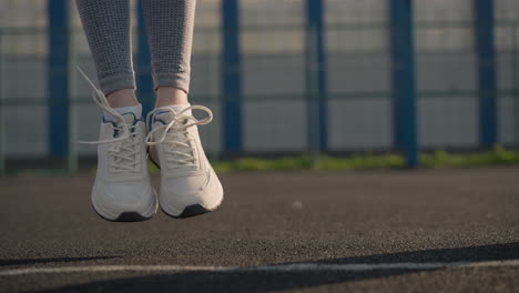 leg view of athletes in athletic wear and canvas shoes jumping on court, with sunlight reflecting off them, creating vibrant highlights, background features building and sports facility