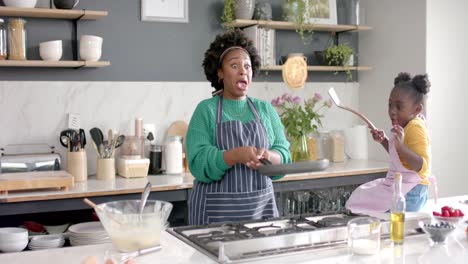 Happy-african-american-mother-and-daughter-frying-pancakes-in-kitchen,-slow-motion