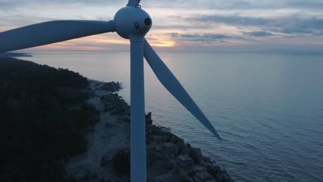 aerial view of abandoned seaside fortification buildings at karosta northern forts on the beach of baltic sea in liepaja, sunset, golden hour, wind turbine in foreground, wide ascending drone shot