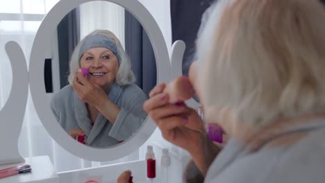 old senior woman grandmother taking care of skin, applying anti-wrinkle foundation with sponge