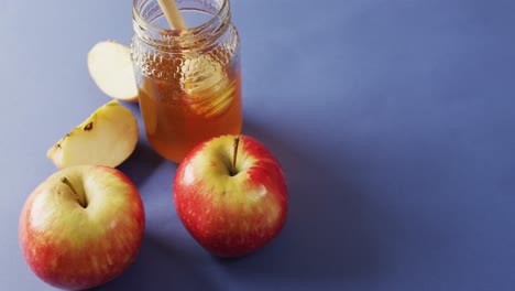 video de miel en frasco, manzanas y rebanadas de manzana sobre una superficie azul
