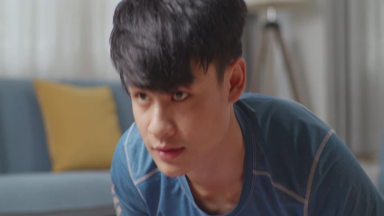 스포츠 옷을 입은 아시아 남성이 집에서 활기차게 밀어붙이는 운동을 하고 있습니다.
