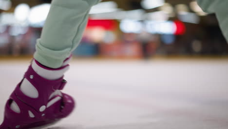 nahaufnahme einer frau, die beim eislaufen auf einer eislaufbahn fällt und lila schlittschuhen und mintgrüne hosen trägt