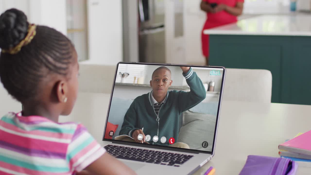 Diverse schoolgirl having laptop video call with male student raising hand in slow motion