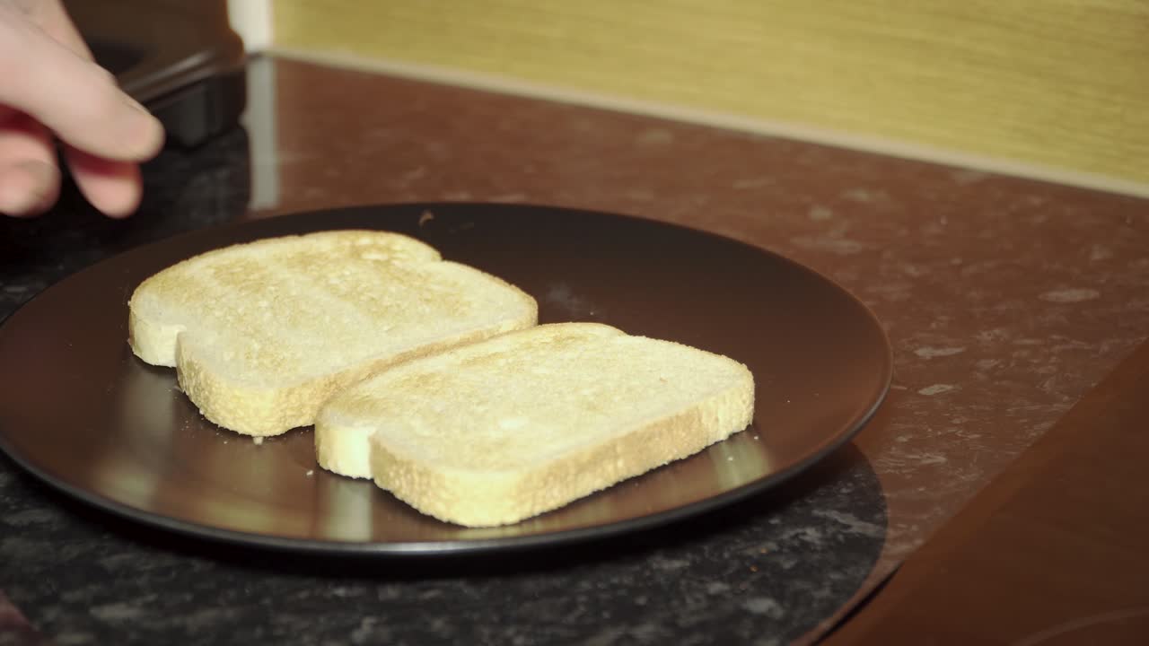 Placing two slices of toast on a black plate on a kitchen bench