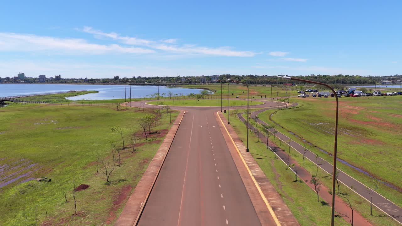 Pickup truck travels a straight road bordered by green space, with glimpses of the Paraná River and Posadas city beyond in Misiones, Argentina