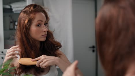 una mujer pelirroja cepillándose el cabello en el baño.