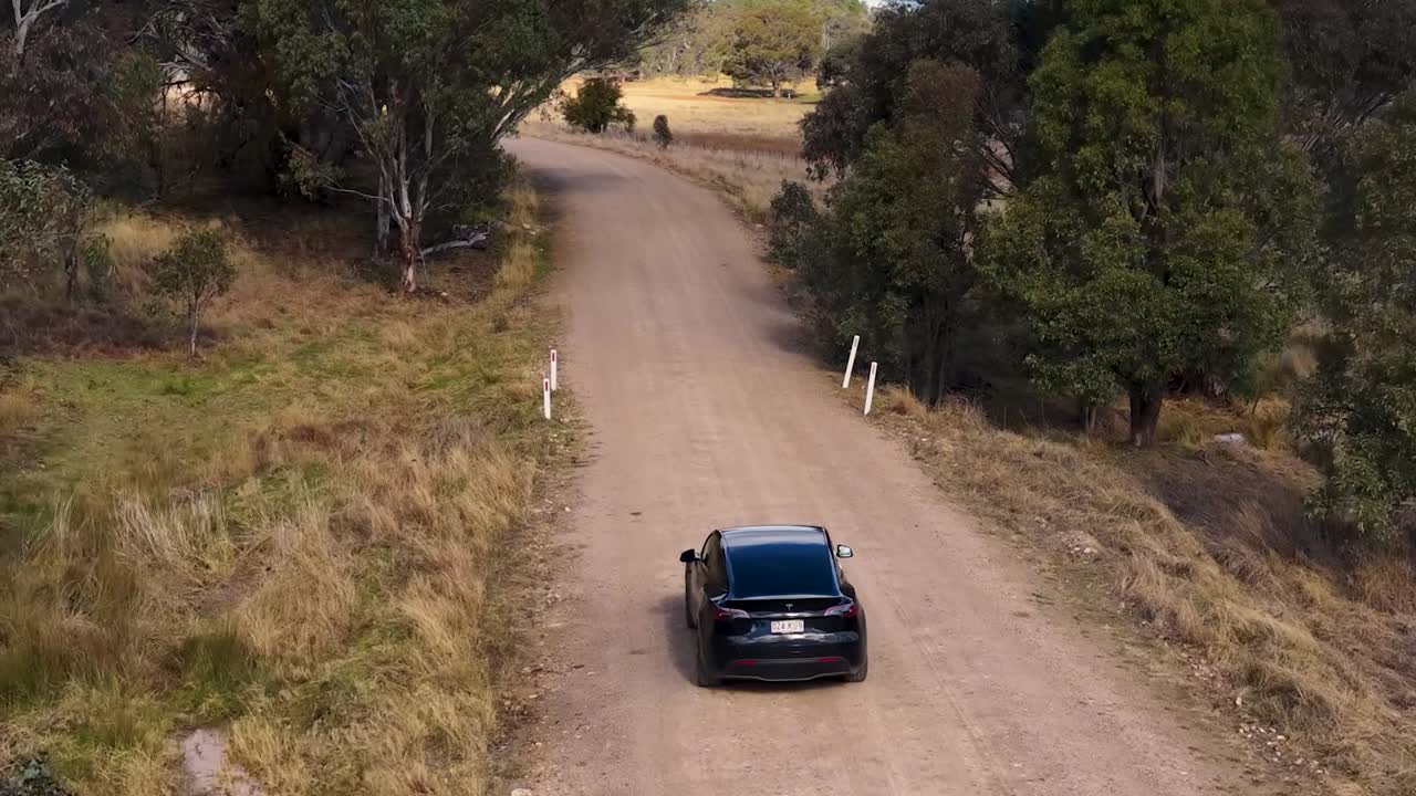 Un drone ad alta angolazione segue un veicolo nero che percorre una remota strada sterrata australiana