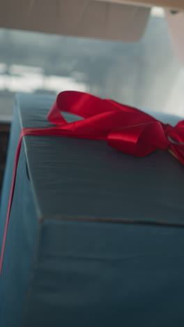man puts hand on large blue present box with red ribbon sitting in light aircraft. secret gift prepared for girlfriend on birthday celebration closeup