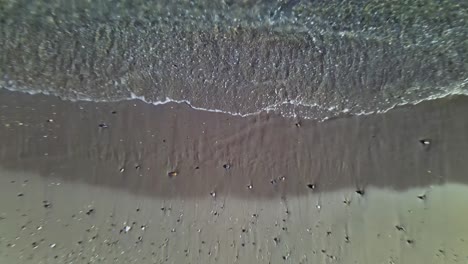 aerial view of close up water and sand on the beach with fast tilt up into a wider view