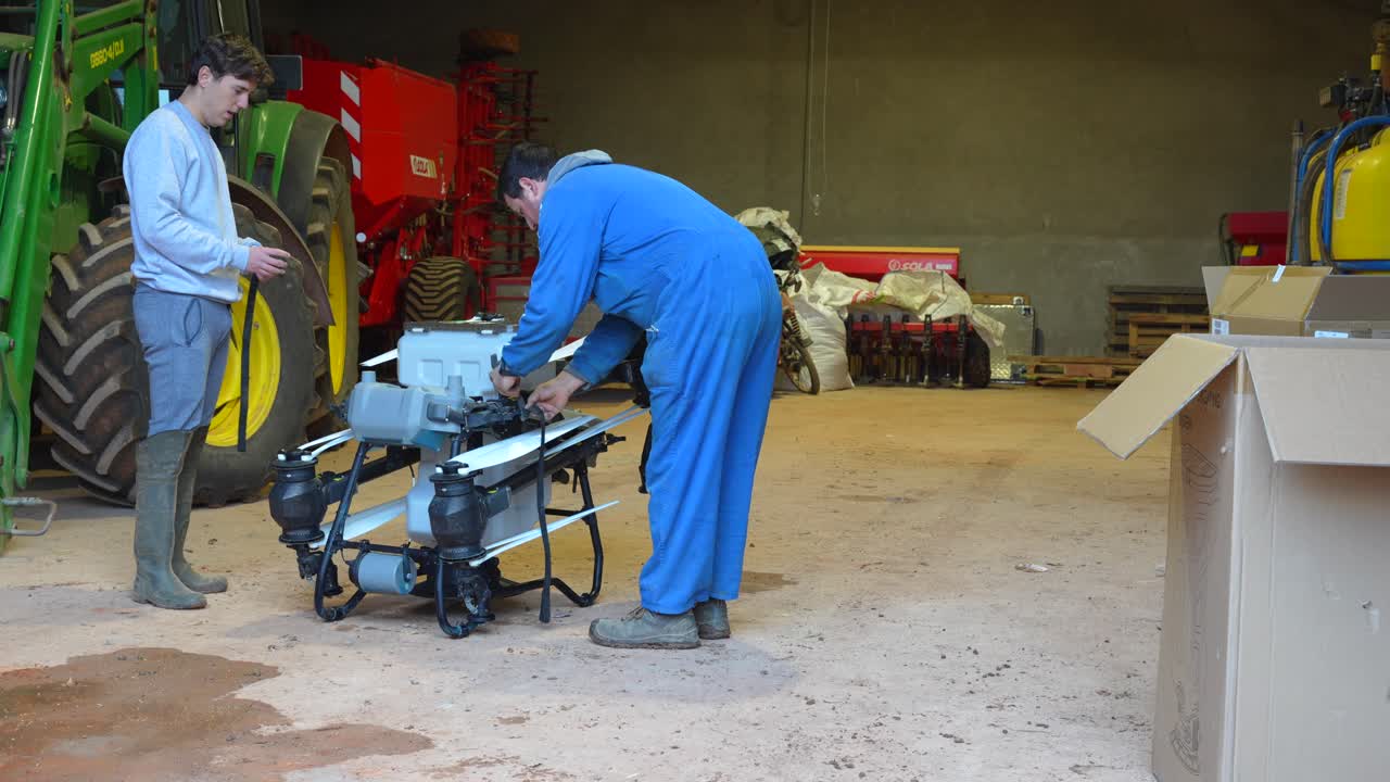 Agricoltori in un fienile fissano le eliche piegate di un drone con elastici per preparare un trasporto sicuro prima del lavoro sul campo.