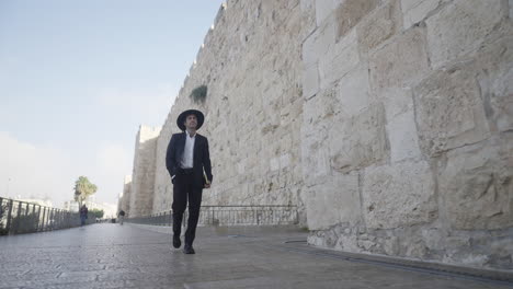 an orthodox male in traditional clothing walks with purpose along the ancient stone walls of the old city of david in jerusalem, reflecting the city's deep history, culture, and spirituality