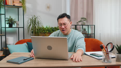 angry asian man use laptop surprised by bad news, fortune loss, game fail, lottery results at home