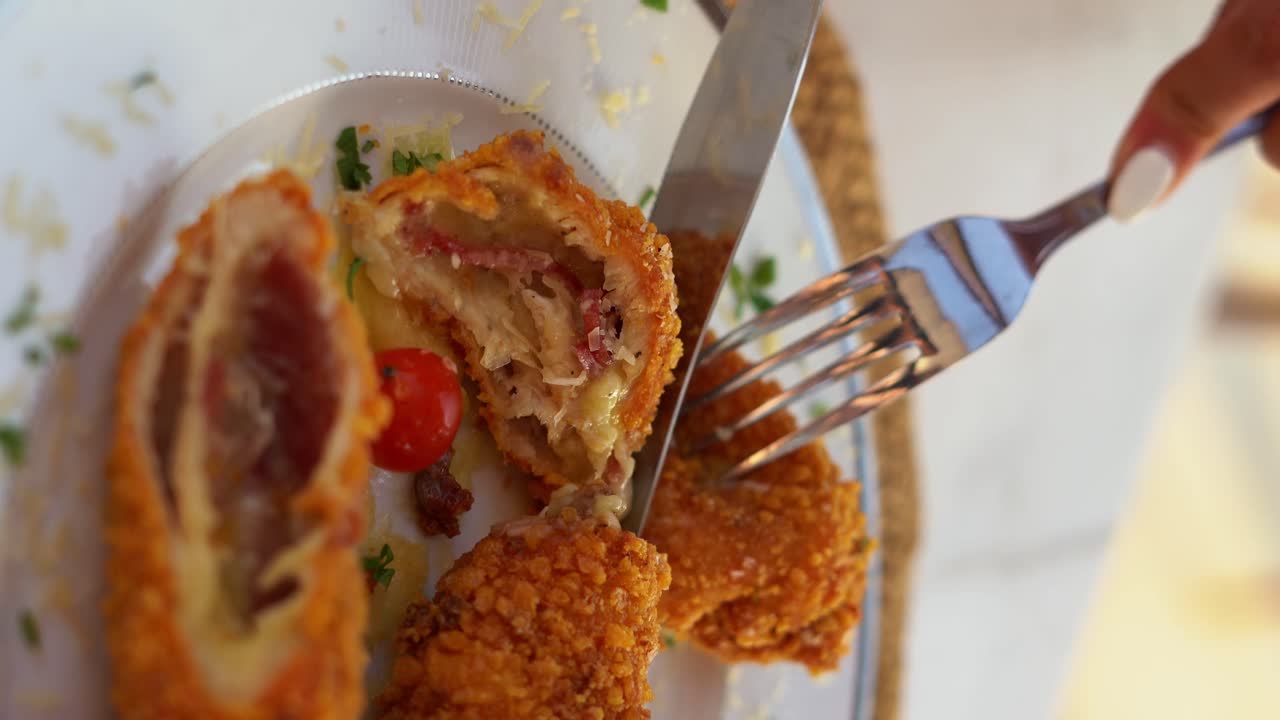 A woman eat her plate that contains a delicious Cordon bleu, close up shot, high angle shot, vertical video