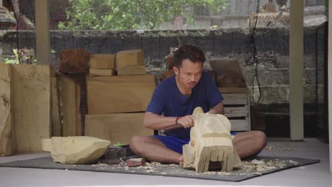 carver asian man hand crafting wooden sculpture sitting in the floor