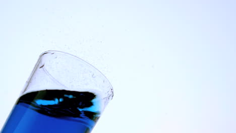 ice falling and missing the glass of blue liquid