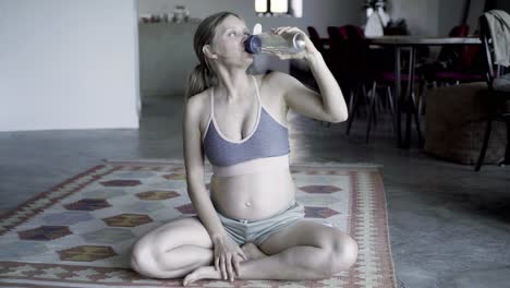 Peaceful-pregnant-woman-sitting-in-lotus-pose-and-drinking-water