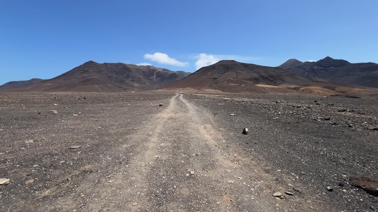 Static shot of the long, empty dirt road leading through the desolate and mountainous landscape of the Jandia Natural Park on the way to Cofete. Fuerteventura, Spain