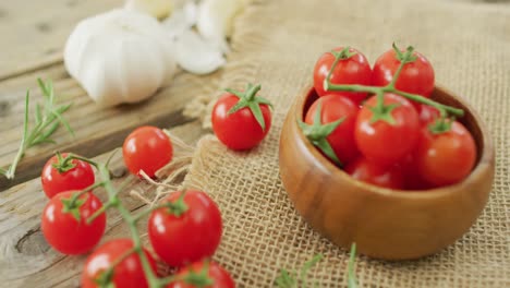 video of fresh cherry tomatoes in bowl and garlic on rustic cloth over wooden background