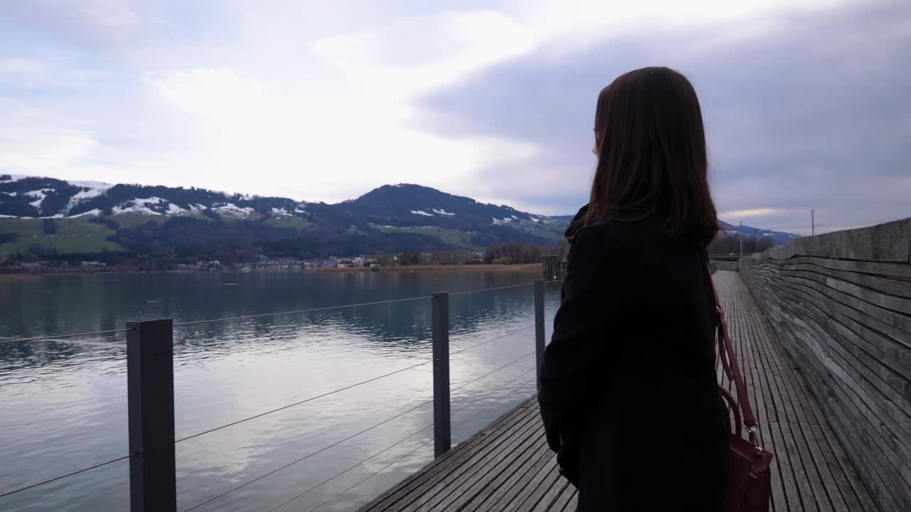 Orbiting shot around a young asian woman sitting on a bench and standing up to enjoy the beautiful view to the lake of Zurich in Rapperswil, Switzerland