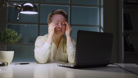 mujer gerente se frota los ojos de la fatiga cuando trabaja en la computadora portátil en la oficina tarde en la noche, exceso de trabajo, horas extras, fecha límite