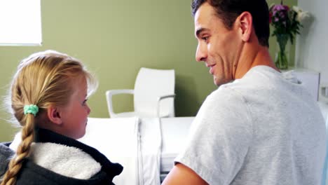 Father-and-daughter-sitting-on-medical-bed-and-talking-to-each-other