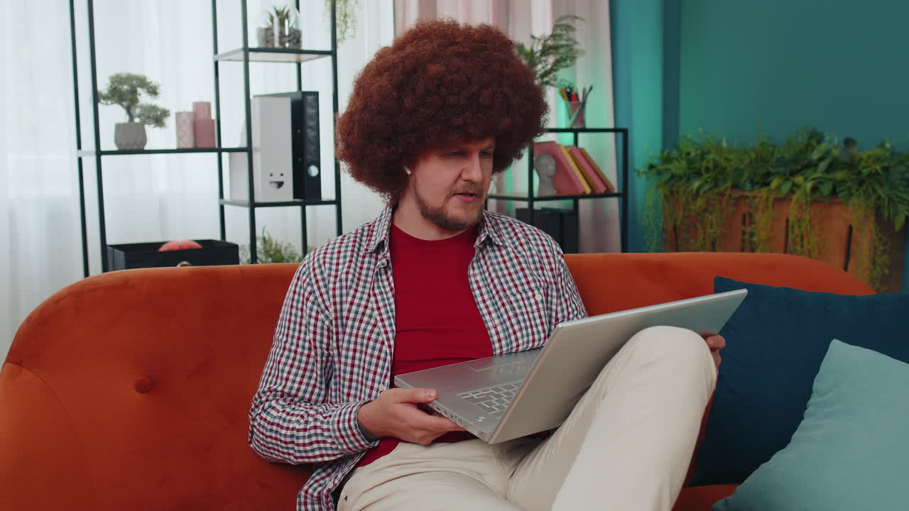 Man sitting on home couch, looking at camera, making video conference call with friends or family