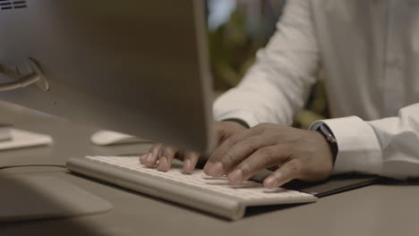 cerca de manos masculinas americanas escribiendo en el teclado de la computadora en el lugar de trabajo