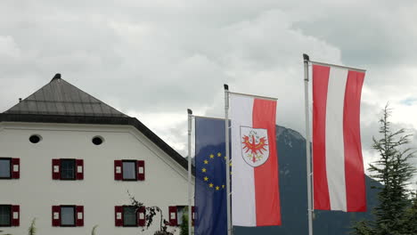 banderas de europa, tirol y austria ondeando en el viento con el hotel al fondo durante el día nublado.