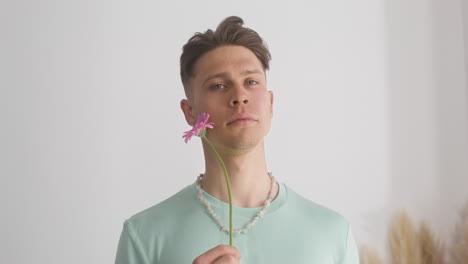 young male model in green t shirt holding flower next to his face