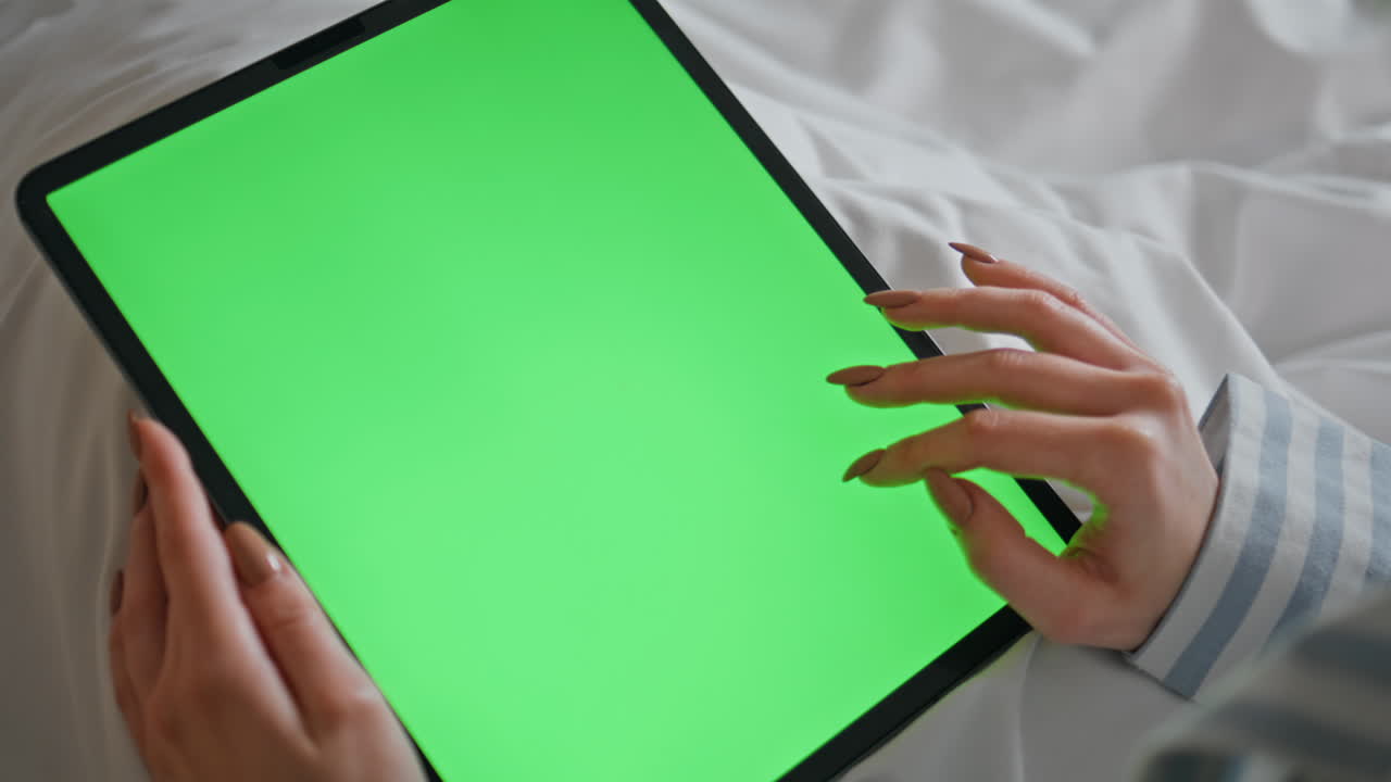 Fingers tapping green screen tablet in bed closeup. Woman hands touching mockup