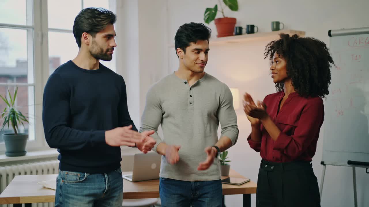Applauding three coworkers responding to good news at office meeting, with laptop and whiteboard