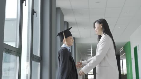 asian mom hugging her son. he's wearing a gown and a mortarboard.