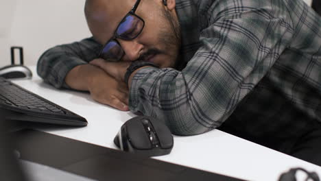 a young indian entrepreneur asleep on his arms slumped over a desk in front of his computer, exhausted from working late putting together his business proposal