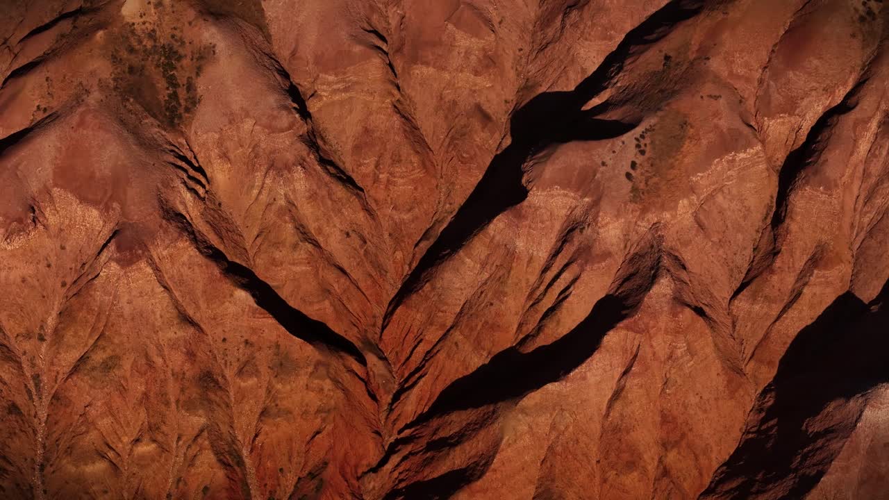Imagem aérea angular e abstrata sobre dobras de rocha afiada e formações de arenito em camadas, estabelecendo a paisagem australiana