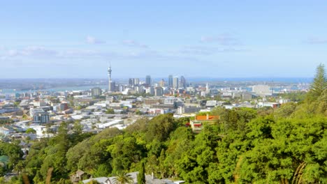 A-travelling-shot-of-the-Auckland-skyline-in-New-Zealand-seen-from-a-distance-with-abundant-vegetation-in-view-on-a-sunny-and-clear-afternoon-with-a-blue-sky